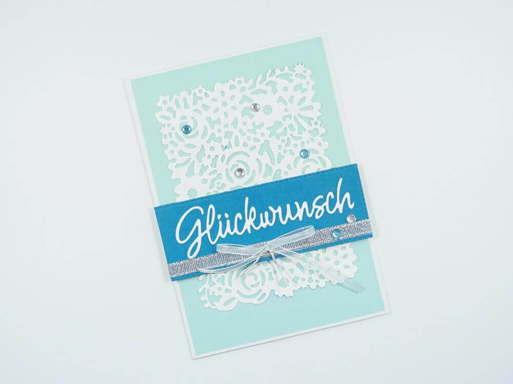 Eine Stanzenshop.de Stanzschablone: Blumenmusterkarte mit blau-weißem Band.