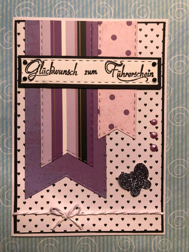 Eine lila Karte mit Punkten und Bändern lässt sich mit der Stanzschablone Fünf lange Wimpel von Stanzenshop.de oder per Hand gestalten. Dieses DIY-Projekt wird mit Sicherheit ein einzigartiges Bastelergebnis ergeben.
