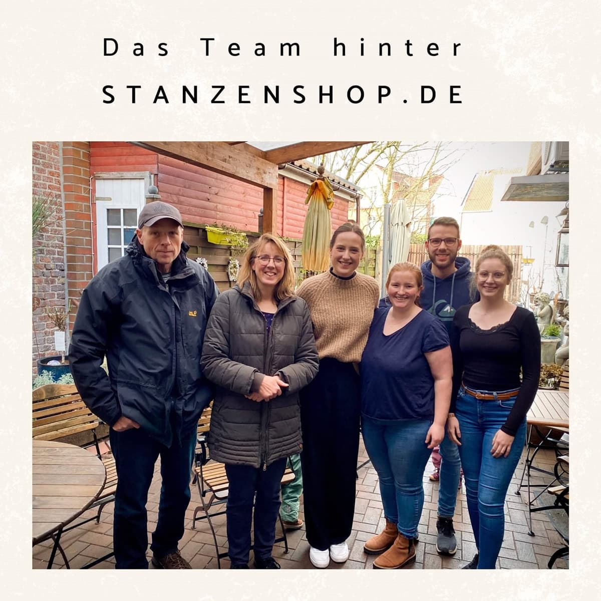 Sechs Personen stehen zusammen in einem Innenhof und posieren für ein Gruppenfoto unter einem Schild mit der Aufschrift "Das Team hinter STANZENSHOP.DE", den Machern der Clear Stamp Weihnachtskatzen & Sprüche von Stanzenshop.de.