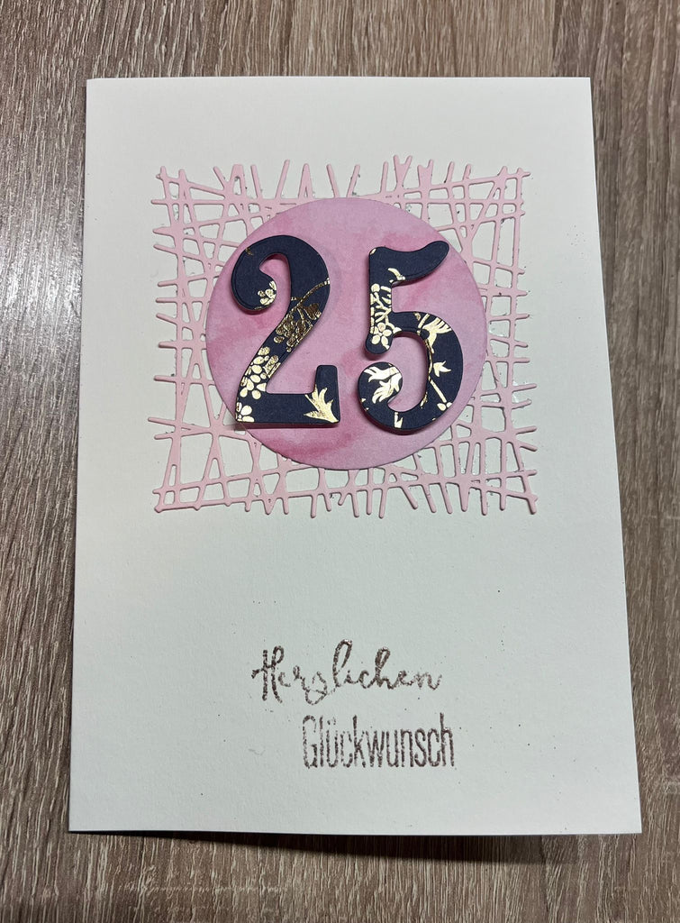 Eine handgemachte Grußkarte mit der Zahl „25“ in dekorativer Schrift und der Aufschrift „Herzlichen Glückwunsch“ darunter, gefertigt mit der Stanzschablone Gittermuster-Technik von Stanzenshop.de, präsentiert auf einer Holzoberfläche.