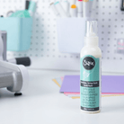 Eine Flasche Sizzix 664576 - Making Essential Express Kleber 120ml von Sizzix steht auf einem Schreibtisch neben farbigem Papier, mit Bastelwerkzeugen, die im Hintergrund verschwimmen - ideal für detaillierte Projekte, die Präzision erfordern.