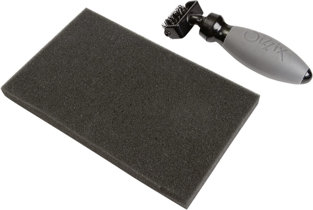 Das Sizzix Stanz-Zubehör-Set "Die Brush & Foam Pad" zeigt eine rechteckige Schaumstoffunterlage (ca. 11,4 x 17,8 cm) neben einer handlichen Bürste mit grauem Griff (ca. 14 x 4 cm) der Marke Sizzix.