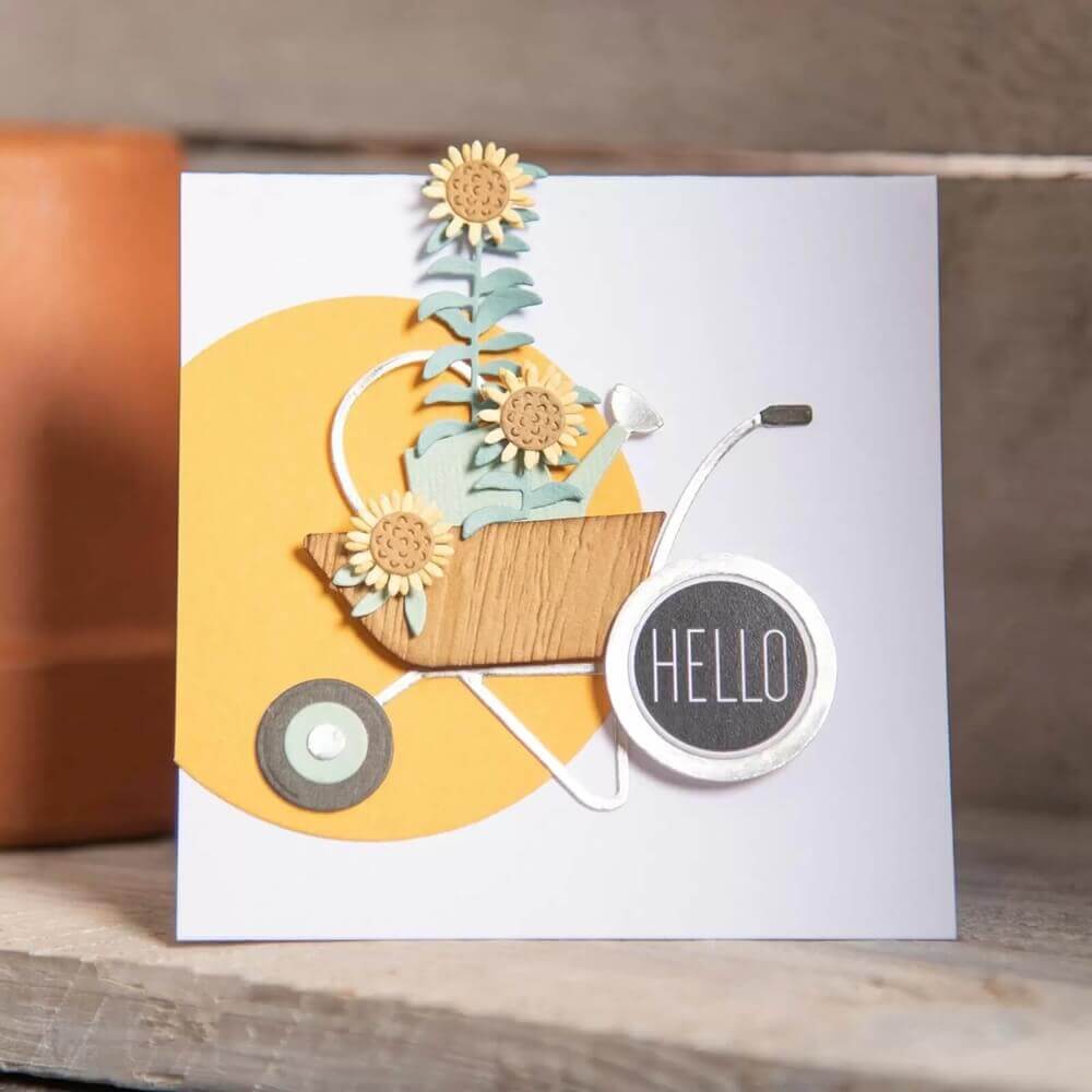 Grußkarte gestaltet mit den Sizzix 664379 Thinlits Stanzschablonen von Sophie Guilar, mit einer Schubkarre, Blumengartenaccessoires und "HELLO" auf dem Rad - perfekt für die Kartenherstellung mit den cleveren Schablonen. Marke: Sizzix.