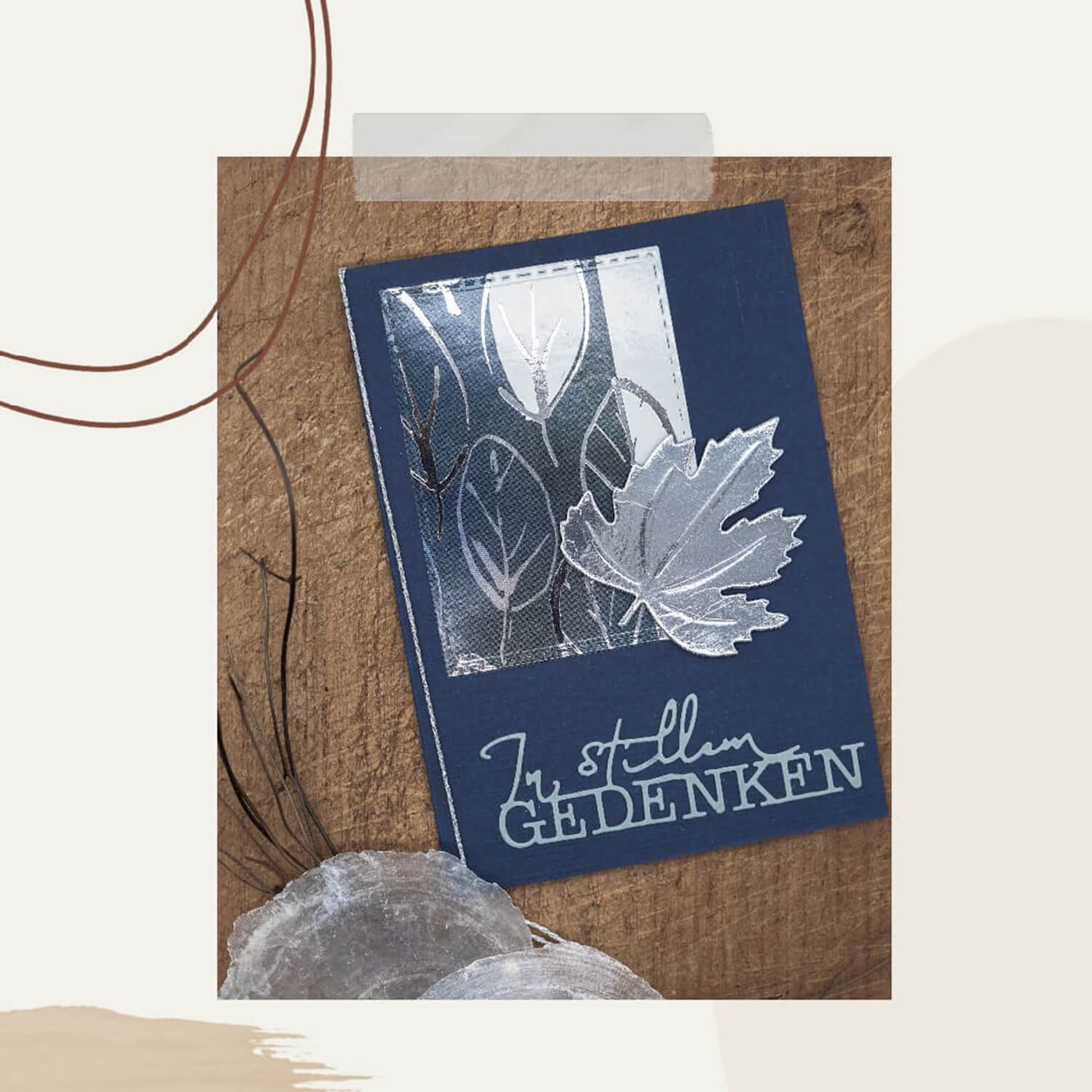 Die Stanzschablone: Ahornblatt von Stanzenshop.de zeigt eine dunkelblaue Grußkarte mit silbernen Blattmotiven und "In stillem Gedenken" auf Deutsch, ideal für Scrapbooking oder Basteln, auf einem braunen strukturierten Hintergrund.