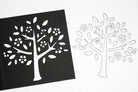 Die Stanzschablone "Baum mit Blüten und Blättern" von Stanzenshop.de liegt neben einem schwarzen Papier-Ausschnitt des Designs - ideal für Bastel- und Scrapbooking-Projekte.