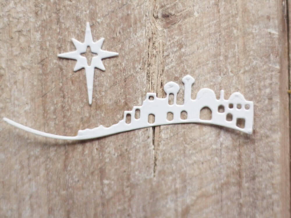 Die "Stanzschablone: Bethlehem mit Weihnachtsstern" von Stanzenshop.de zeigt ein weißes Stadtbild und den Stern von Bethlehem auf strukturiertem Holz, perfekt für Winterbasteln oder Kartengestaltung in Ihren liebsten Weihnachtsprojekten.
