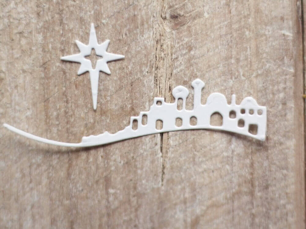 Ein Papierausschnitt aus einer Stanzschablone: Bethlehem mit Weihnachtsstern-Krippe auf einer Holzoberfläche von Stanzenshop.de.