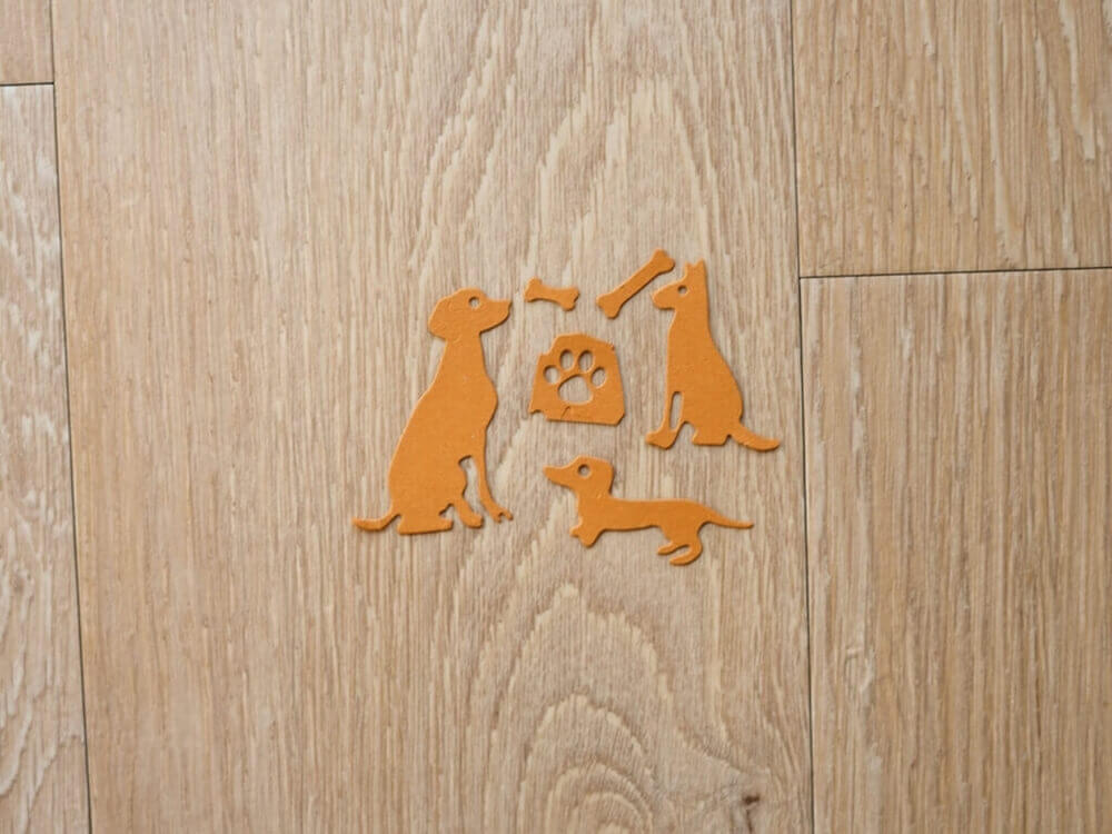 Ein Satz Stanzschablonen: Drei Hunde-Silhouetten auf einem Holzboden von Stanzenshop.de.