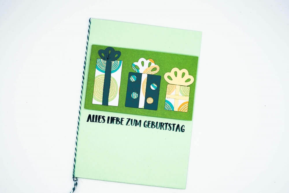 Ein grünes Stanzenshop.de-Notizbuch mit einer Geschenkbox „Drei verschiedene Geschenke“ mit preiswerten Stanzschablonen.