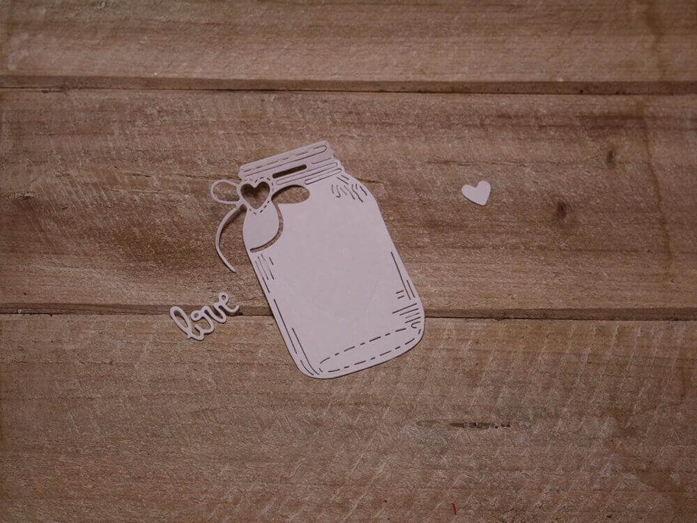 Eine Stanzschablone Glas mit Herz und Schriftzug Love von Stanzenshop.de ausgeschnitten auf einem Holztisch.