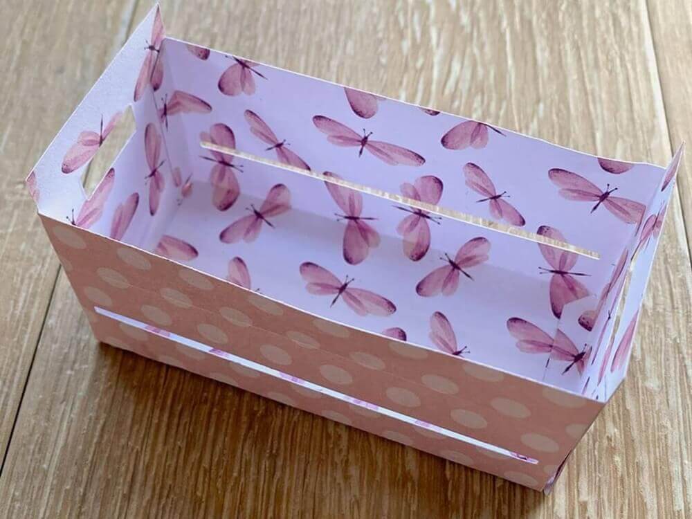 Eine kleine rechteckige Geschenkbox Hochzeit, hergestellt mit der "Stanzschablone: Großer Karton" von Stanzenshop.de mit rosa Libellen- und Tupfenmuster auf einer Holzunterlage.