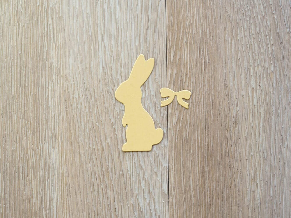 Eine gelbe Stanzschablone: Hase mit einer Fliege mit Schleife auf einem Holztisch von Stanzenshop.de.
