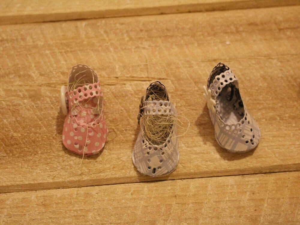 Drei kleine, handgefertigte Puppenschuhe - rosa mit weißen Tupfen und blauen Mustern - sitzen auf Holz und bieten Inspiration für die Verwendung der Stanzenshop.de Stanzschablone Kinderschuh für ein Baby in Ihrem nächsten Scrapbooking-Projekt.