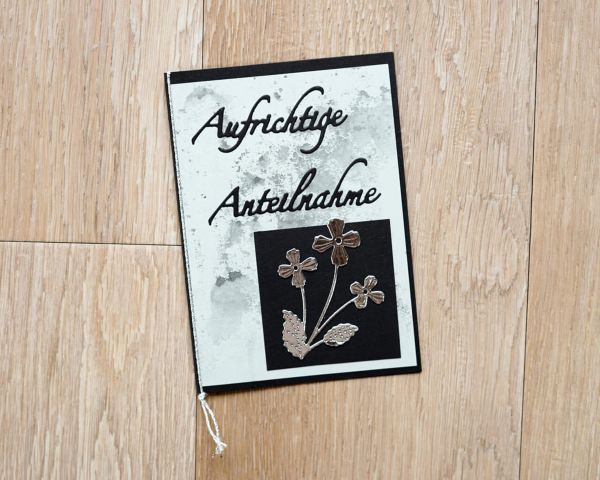 Eine Kondolenzkarte mit "Aufrichtige Anteilnahme" und der Stanzenshop.de Stanzschablone: Kleine Blume mit drei Blüten Design, ideal zum Basteln oder Scrapbooking, liegt auf einer Holzunterlage.