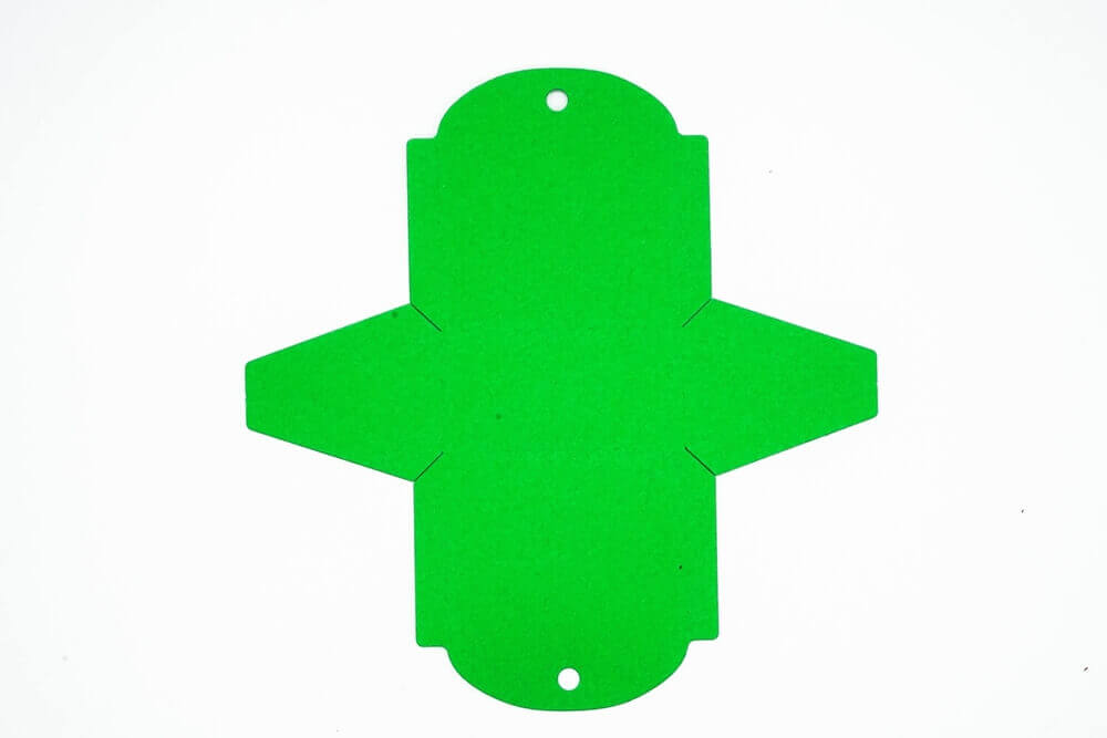 Ein grünes Papierkreuz mit einem Loch in der Mitte, erstellt mit einer Stanzschablone Kleine Tischkarte Schachtel von Stanzenshop.de.