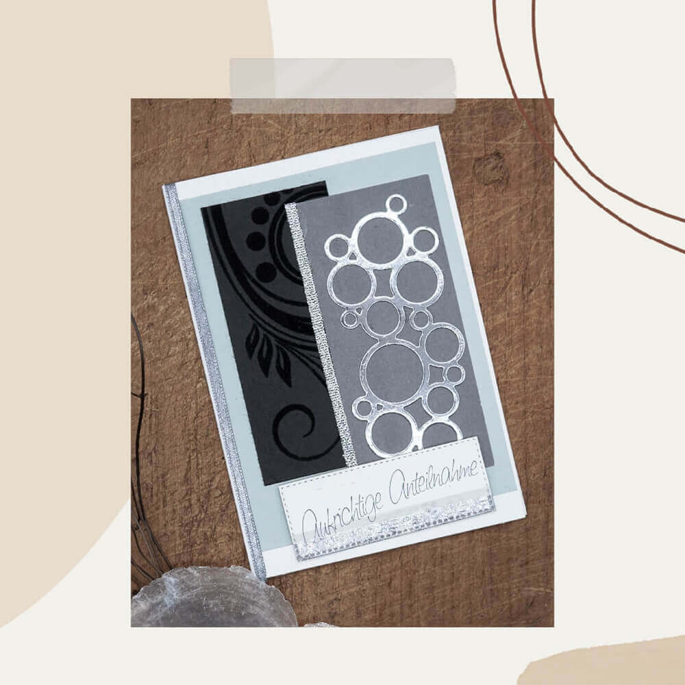 Eine handgefertigte grau-schwarze Karte mit silbernen Kreisen, die mit der Stanzschablone Mehrere Kreise aneinander von Stanzenshop.de erstellt wurden, und dem deutschen Text "Herzliche Anteilnahme" - ideal für Scrapbooking- oder Bastelprojekte.