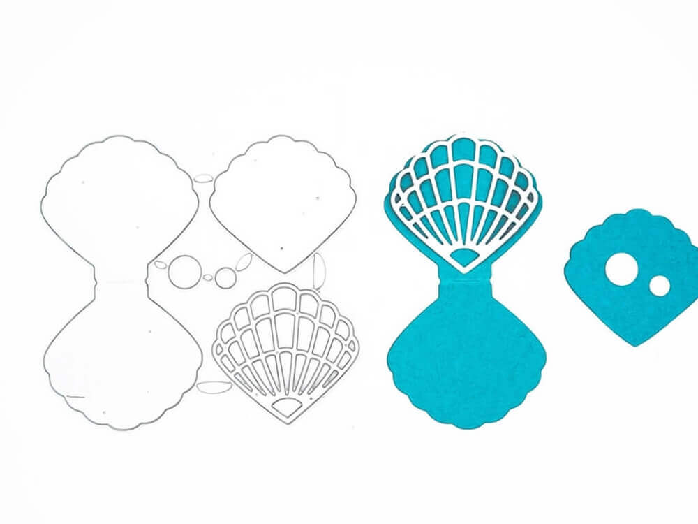 Die Stanzschablone Muschel zum Aufklappen von Stanzenshop.de zeigt mit ihren blauen Papierausschnitten auf weißem Hintergrund Muschelformen in verschiedenen Stadien - ein ideales Bastelergebnis für kreative Gastgeschenke.