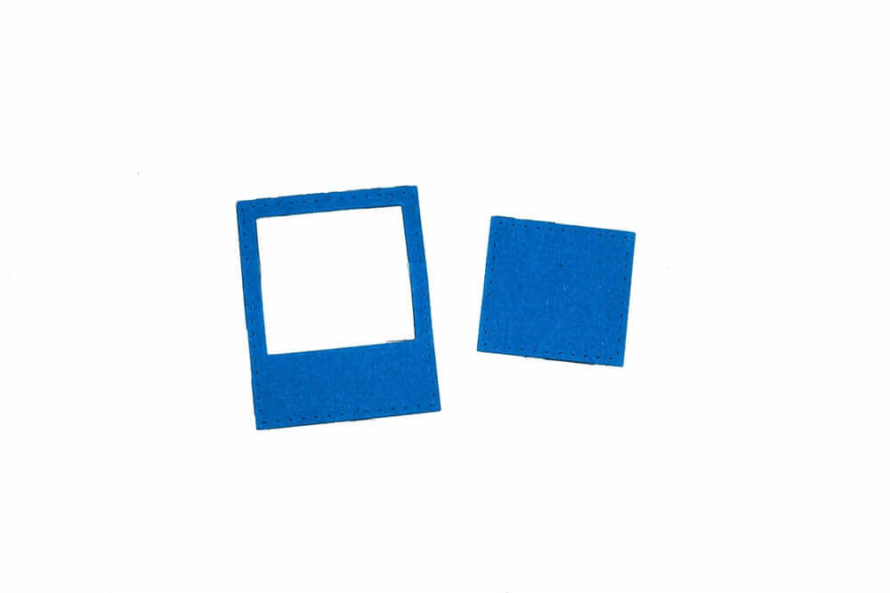 Eine blaue "Stanzschablone Rahmen für Polaroidbild" von Stanzenshop.de mit einem ausgeschnittenen Zentrum sitzt neben einem einfarbig blauen Quadrat - ideal für Scrapbooking oder Basteln mit Ihrer Lieblingsstanze auf weißem Hintergrund.