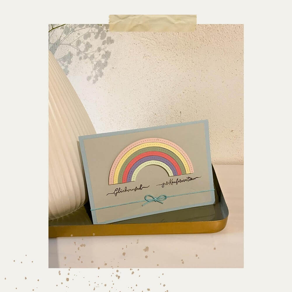Eine handgefertigte Karte mit pastellfarbenem Stanzschablone-Regenbogen von Stanzenshop.de und eleganter Schrift liegt auf einem goldenen Tablett, eine Vase mit floralem Akzent rundet die Szene ab - die ideale Inspiration für dein nächstes Bastelergebnis.