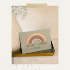 Eine handgefertigte Karte mit pastellfarbenem Stanzschablone-Regenbogen von Stanzenshop.de und eleganter Schrift liegt auf einem goldenen Tablett, eine Vase mit floralem Akzent rundet die Szene ab - die ideale Inspiration für dein nächstes Bastelergebnis.