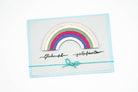 Eine Grußkarte mit einem geschichteten Regenbogendesign mit der Stanzschablone Regenbogen von Stanzenshop.de, handgeschriebenem deutschen Text und einer blauen Schleife - ein inspirierendes Bastelergebnis, kompatibel mit gängigen Stanzmaschinen.