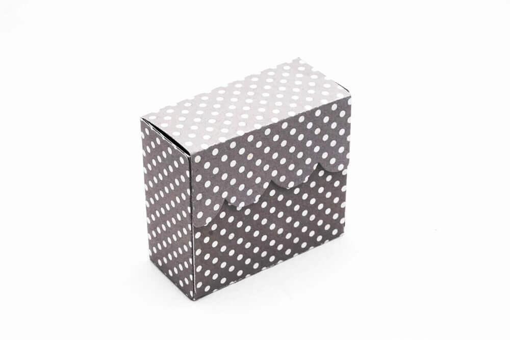 Eine schwarz-weiß gepunktete Stanzschablone Schachtel mit Verschluss von Stanzenshop.de auf einer weißen Fläche.