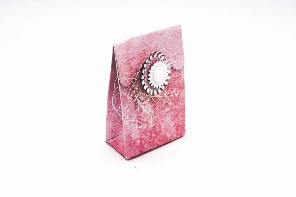 Eine kleine rosa Geschenktüte, verziert mit einer Blume aus der Stanzschablone Schachtel mit Verzierungen von Stanzenshop.de und Kordel auf der Vorderseite, perfekt für Gastgeschenke, dargestellt auf weißem Hintergrund.