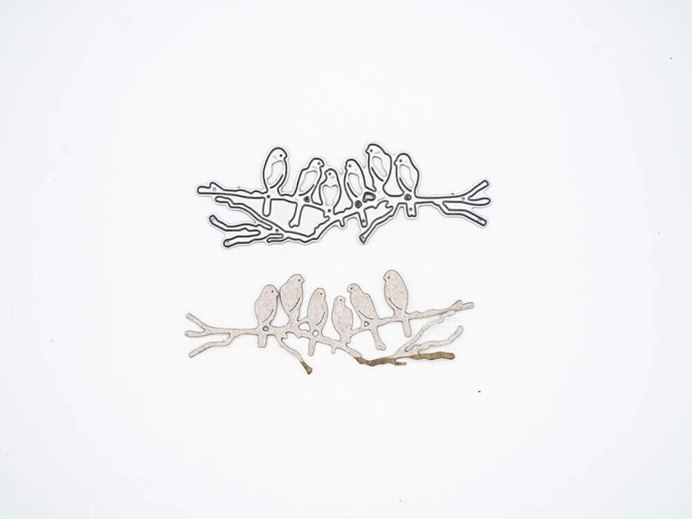 Zwei Metallausschnitte - ein silberner und ein goldener - zeigen sechs Vögel auf einem Zweig. Ideal für die "Stanzschablone: Sechs Vögel auf einem Ast" von Stanzenshop.de für Scrapbooking oder Kartenherstellung Projekte. Dargestellt auf einem schlichten weißen Hintergrund.
