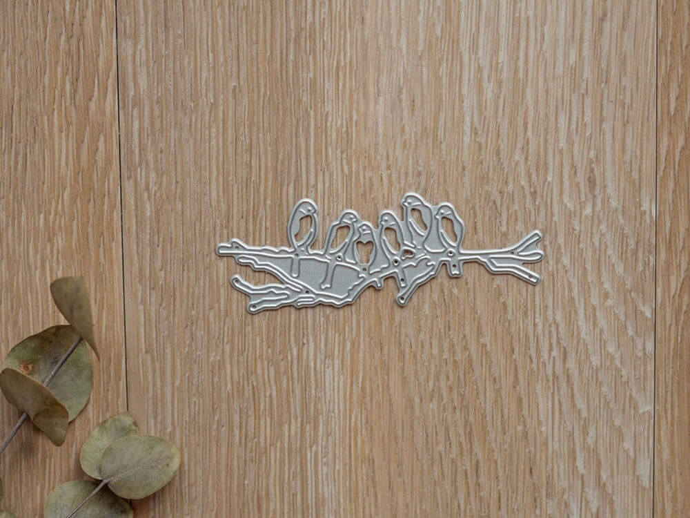 Die Stanzenshop.de "Stanzschablone: Sechs Vögel auf einem Ast" ist eine Stanze auf Holz mit getrockneten Blättern - ideal für Scrapbooking oder Kartenherstellung.