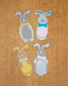 Vier Papier-Osterhasen mit Fliege in bunten Farben, arrangiert auf Holz - ideal zum Basteln zu Ostern mit der Stanzschablone "Süßer Osterhase" von Stanzenshop.de.