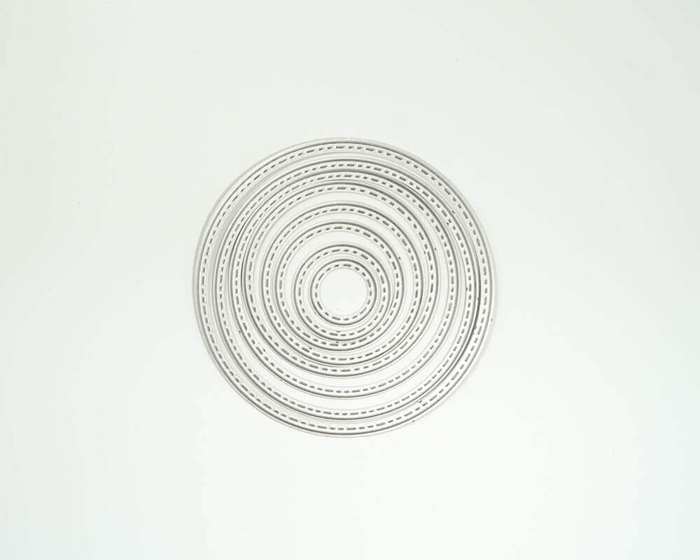 Die "Stanzschablone: Sieben Kreise mit gestricktem Rahmen" von Stanzenshop.de zeigt konzentrische Metallringe mit dekorativen Rändern, ideal für Scrapbooking und Basteln, in einem kreisförmigen Muster auf einem schlichten weißen Hintergrund.