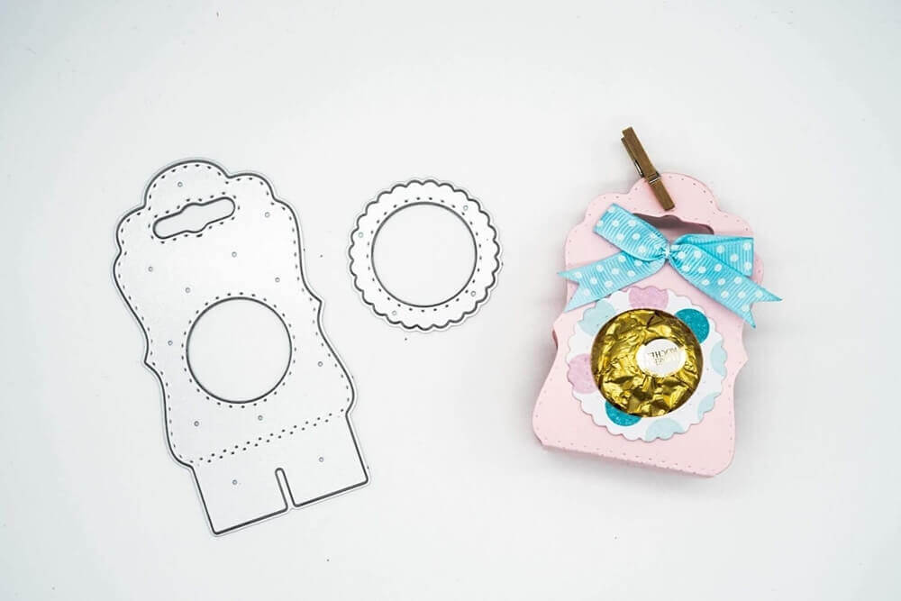 Die Stanzschablone Tischkarte mit Kreis von Stanzenshop.de ist mit einem fertigen rosa Geschenkkarton, einer blauen Tupfenschleife und in Gold verpackten Süßigkeiten abgebildet - ideal für Scrapbooking oder jedes Bastelset-Projekt.