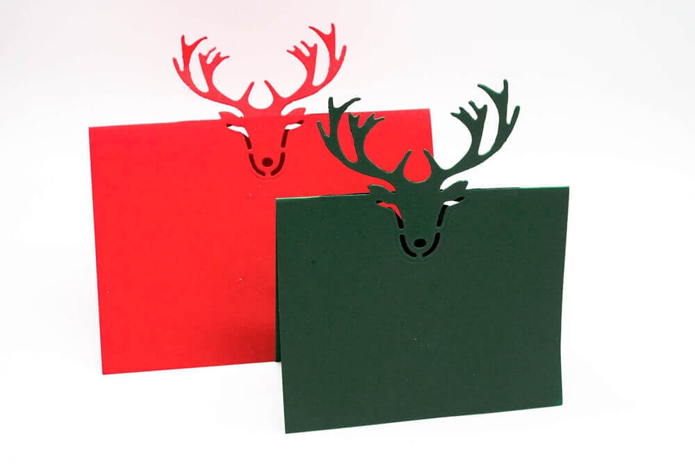 Die Stanzschablone: Tischkarte Rentierkopf von Stanzenshop.de zaubert rote und grüne Klappkarten mit einem Rentierkopf-Ausschnitt - ideal für Tischkarten basteln oder kreative Scrapbooking-Projekte.