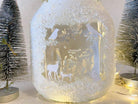 Ein Glasgefäß mit weißen Silhouetten von Rehen und Vögeln aus der Stanzschablone Wald mit Tieren von Stanzenshop.de, umgeben von Kunstschnee und Mini-Tannenbäumen - ein reizvolles Bastelergebnis für winterliches Scrapbooking.