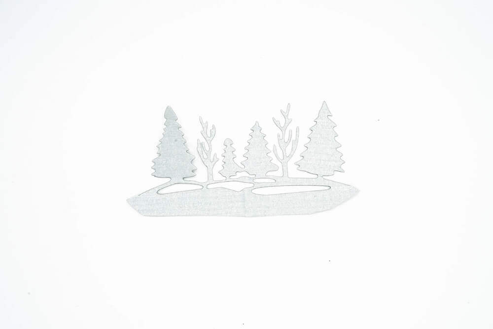 Ein weißes Stanzenschop.de-Blatt mit Waldlandschaft im Winterbäumen darauf, unter Verwendung von Stanzschablonen.