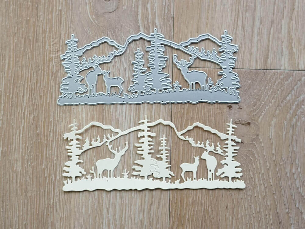 Ein Paar Stanzschablonen Winterlandschaft mit Bergen und Tieren von Stanzenshop.de auf einem rustikalen Holzboden, perfekt für eine gemütliche Winteratmosphäre.