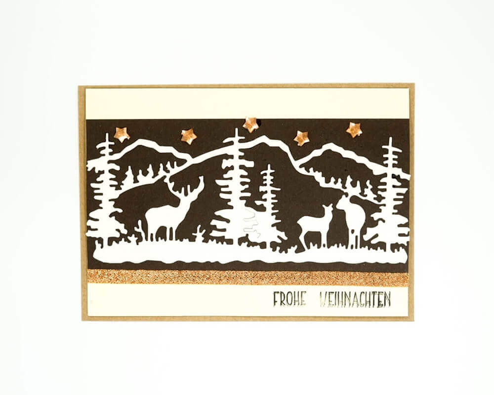 Eine Winterkarte mit der Silhouette eines Hirsches inmitten von Bäumen, gefertigt mit der Stanzschablone Winterlandschaft mit Bergen und Tieren von Stanzenshop.de.
