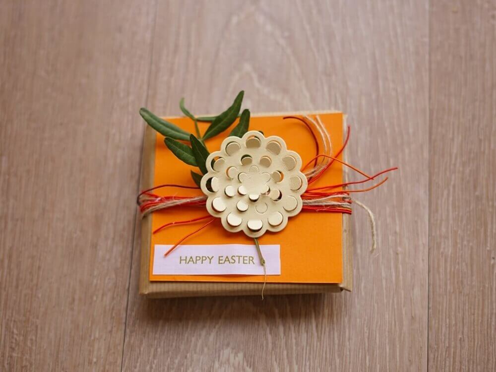 Eine orangefarbene Stanzschablone-Geschenkbox mit einer Blume darauf von Stanzenshop.de.
