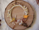 Ein Holzkranz mit Papierblättern, zwei gelben Vögeln, Federn und Trockenblumen auf einer Holzscheibe - ideal für Scrapbooking oder Kartengestaltung mit der Stanzenschablone Zwei Kreise mit Blumen von Stanzenshop.de.