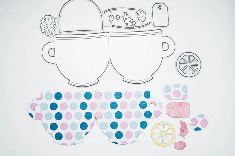 Gestanzte Formen aus der Stanzschablone Zwei Tassen mit Zubehör von Stanzenshop.de: zwei Teetassen, eine Zitronenscheibe, Anhänger und florale Elemente sind auf einem weißen Hintergrund zum Basteln angeordnet.