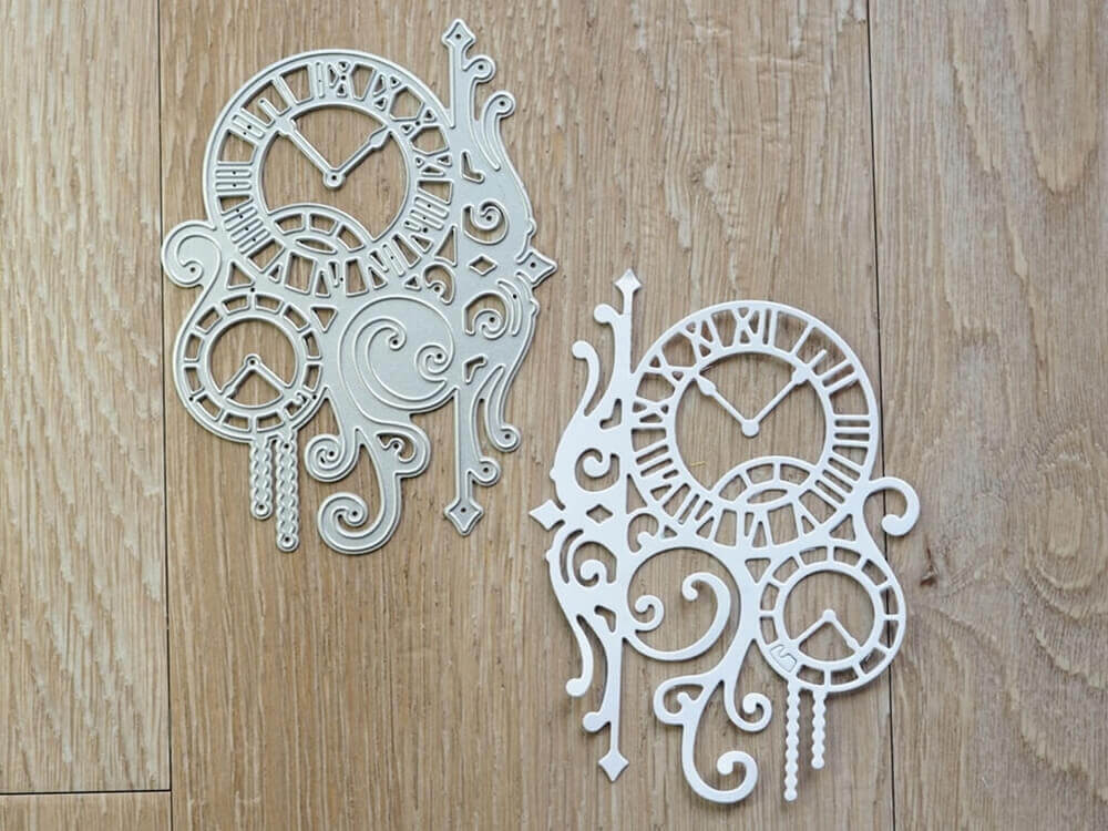 Die "Stanzeschablone Zwei Uhren mit Ranken" von Stanzenshop.de bietet zwei verschnörkelte Ziffernblattausschnitte aus Metall mit römischen Ziffern, ideal um Scrapbooking- oder Bastelprojekte mit Vintage-Details zu versehen.