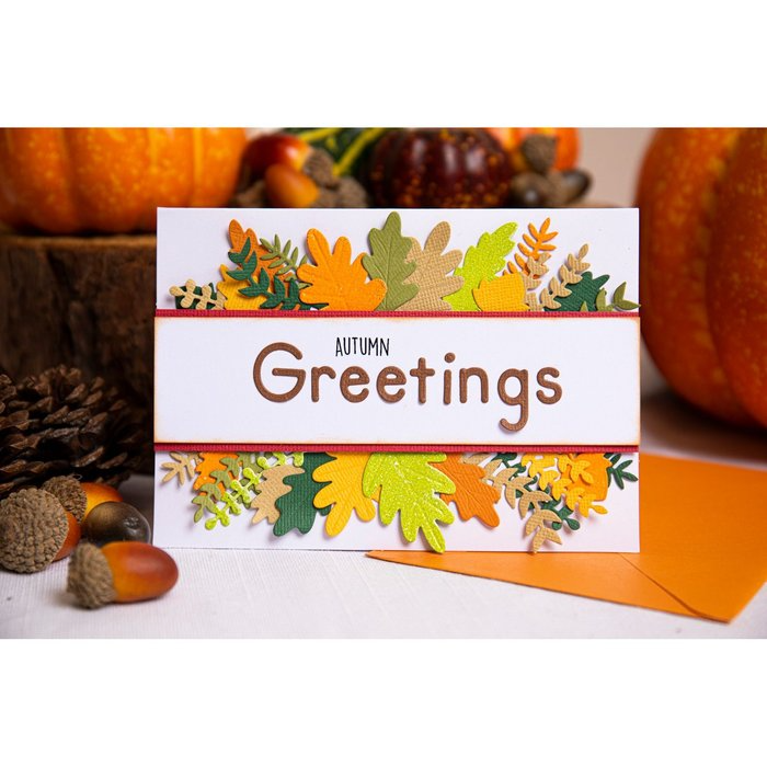 Die Karte Sizzix 665952 - Thinlits Harvest Squirrels von Sizzix zeigt Herbstblätter und Eicheln, "Autumn Greetings" in der Mitte, mit Kürbissen und drei Tannenzapfen im Hintergrund. Kartengröße ist 9x8 Zoll.