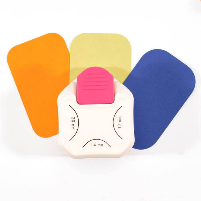 Der Vaessen Creative - 3-in-1 Eckenstanzer 14-17-20mm von Vaessen Creative sitzt auf orangefarbenem, gelbem und blauem, rechteckigem Papier - ideal für die Gestaltung abgerundeter Ecken bei Ihren Bastelarbeiten.