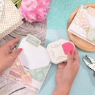 Mit dem Vaessen Creative - 3-in-1 Eckenstanzer 14-17-20mm rundet eine Person die Ecken einer floralen Geburtstagskarte ab, während andere Bastelmaterialien und Umschläge von Vaessen Creative auf dem Tisch liegen.